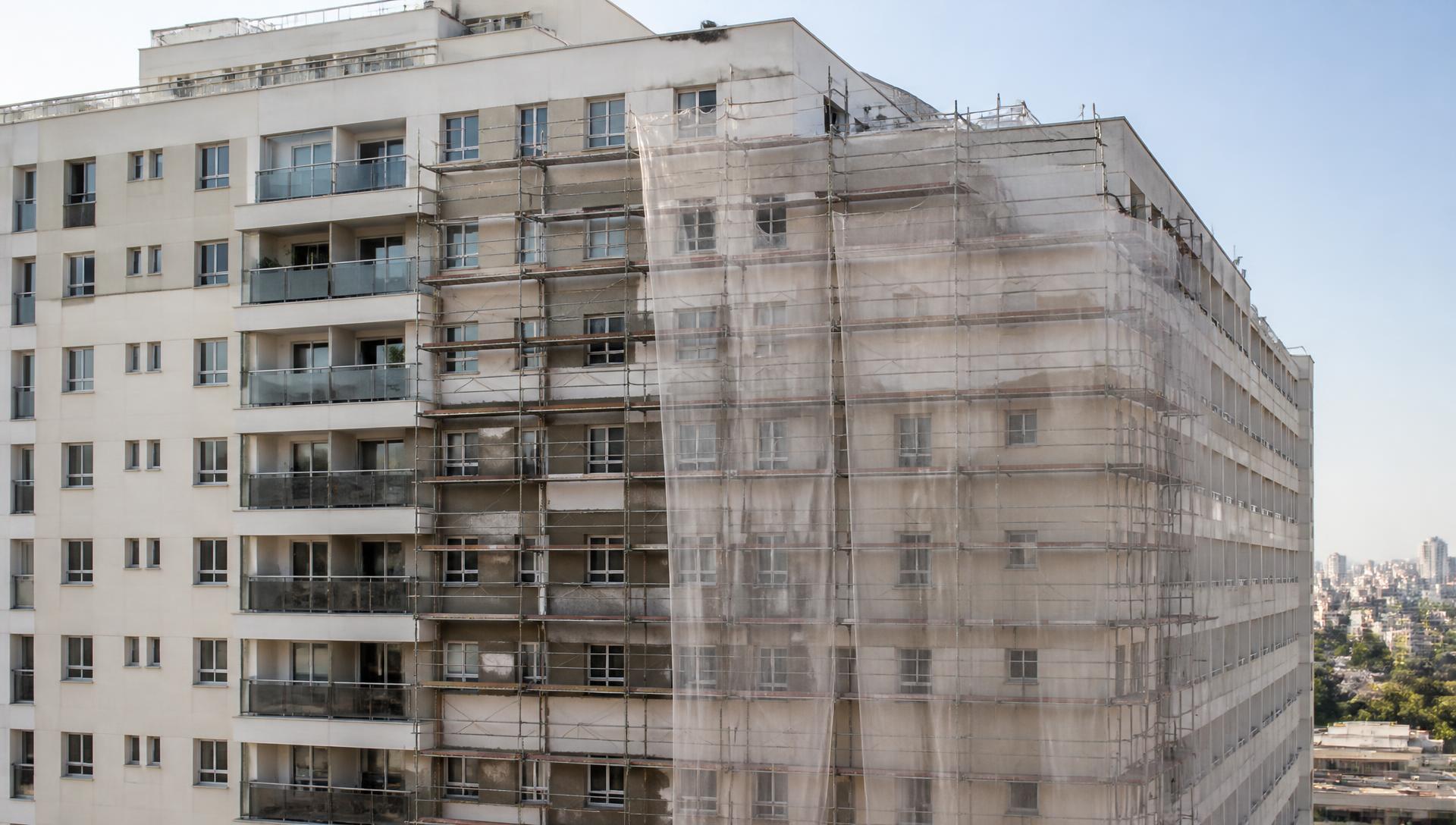 Fachada de condomínio residencial em obra de reforma, com andaime e tela de proteção